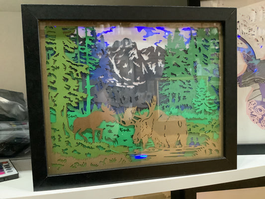 8 x 10” black shadow box with paper cut moose in mountain scene with lights