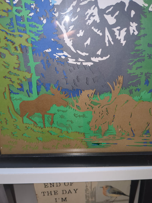 8 x 10” black shadow box with paper cut moose in mountain scene with lights